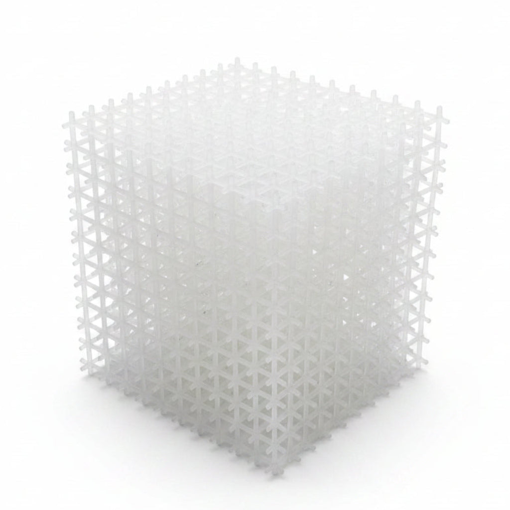 A white plastic biofilm reactor media cube with a cross-shaped grid structure, resting on a wooden surface.