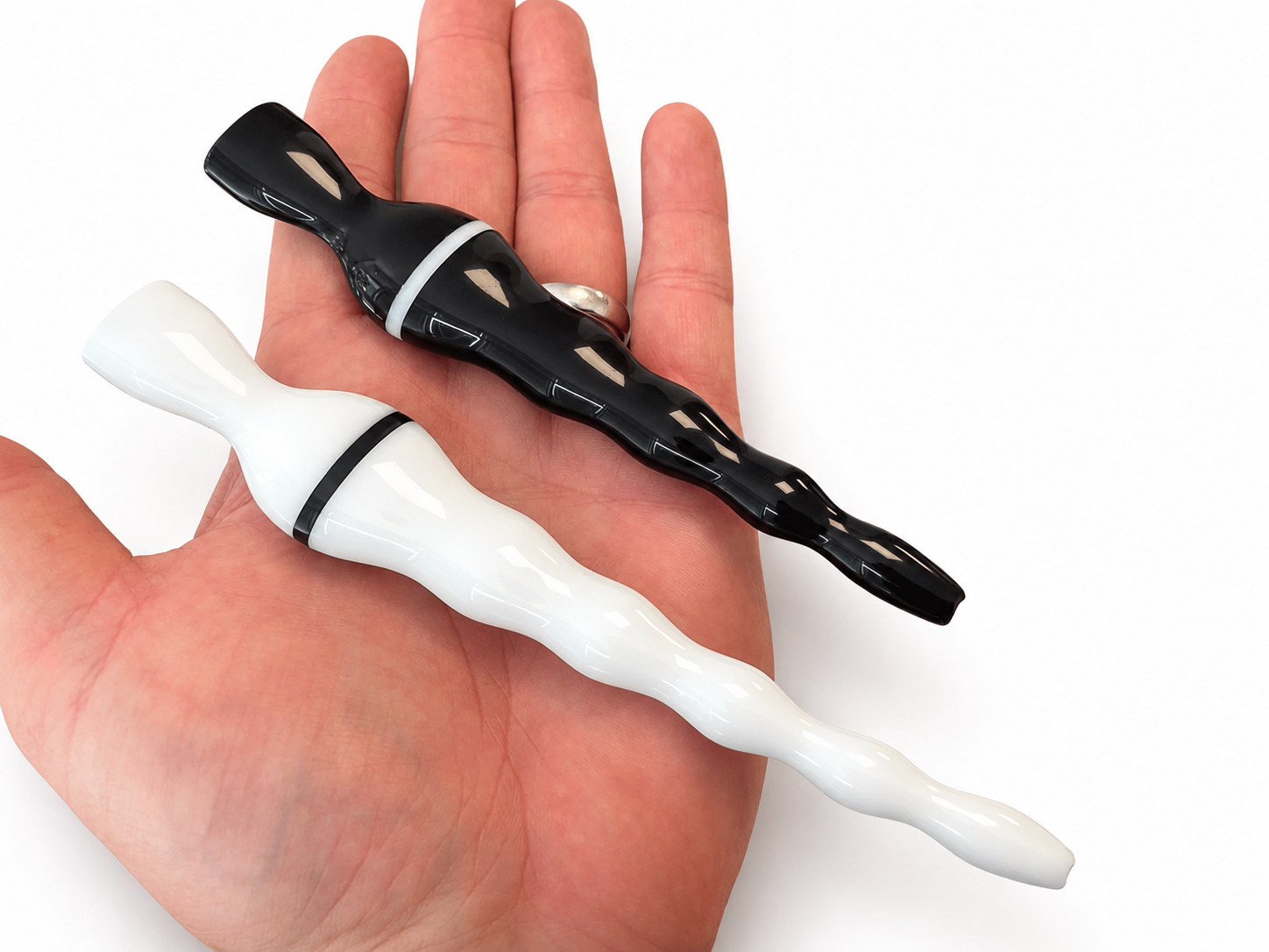 Glossy printed tapered wavy rods, one black and one white, held in an open hand for scale