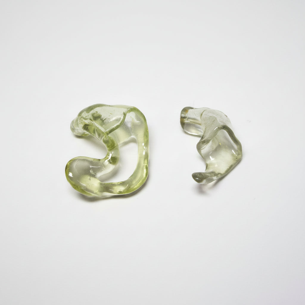 Two translucent olive-green glass earpieces or hearing aid components on a plain light gray background.