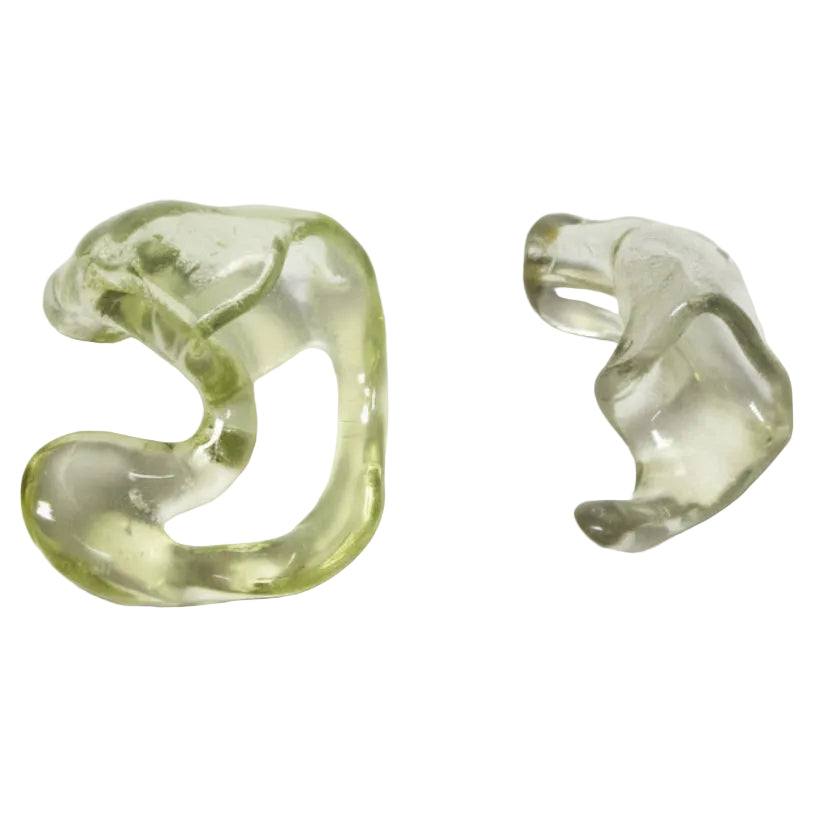 Two translucent olive-green glass earpieces or hearing aid components on a plain light gray background.